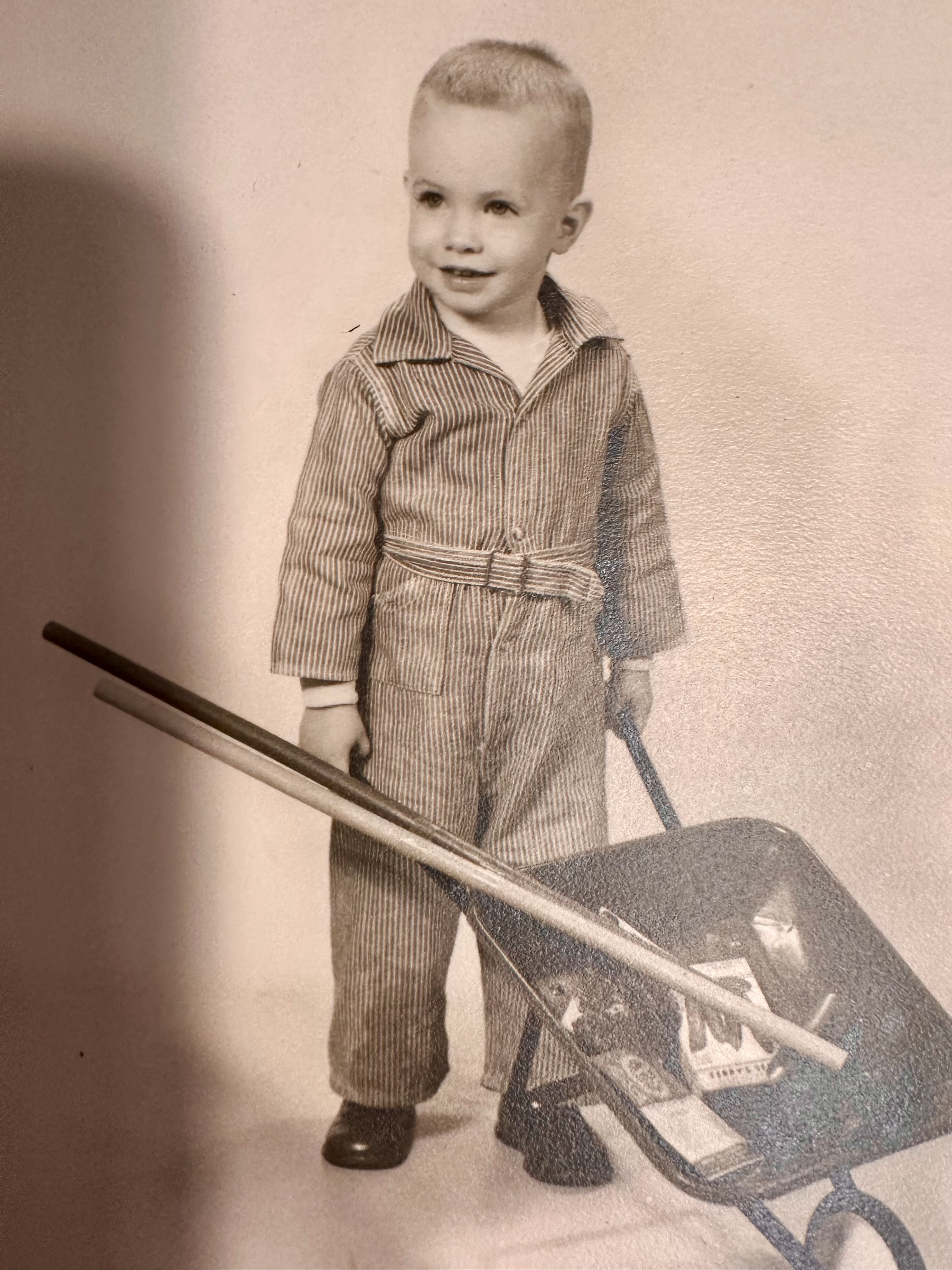 Young Dirk Adams standing beside a toy wheelbarrow.